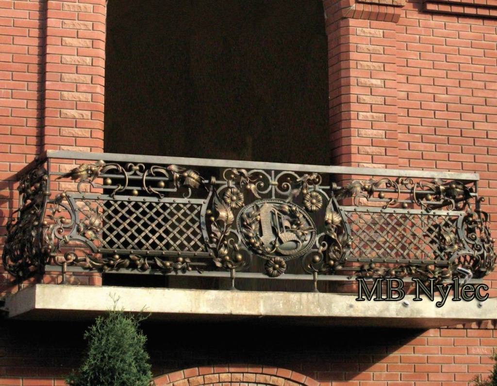 Massive blacksmith balcony railing BA43 with a diagonal lattice and a gilded central medallion on red brick