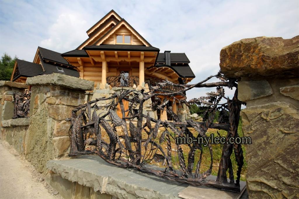 Forged plant fence BM42 with grasses on a stone wall beside a log house