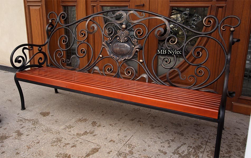 Forged bench MK1B with a coat of arms in the backrest in front of a wooden door