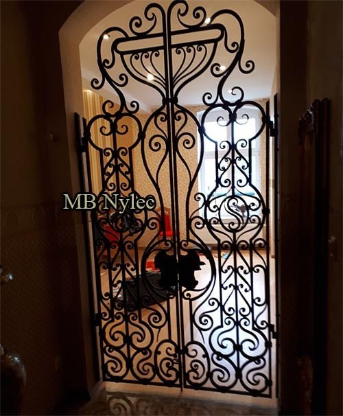 Openwork forged door grille DZ4 in an arched opening lit from behind