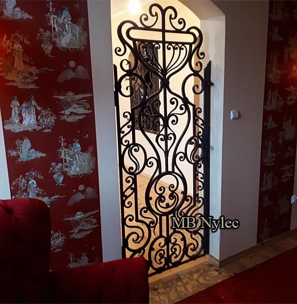 Forged grille in the DZ4 pattern framing a mirror on a red patterned wall