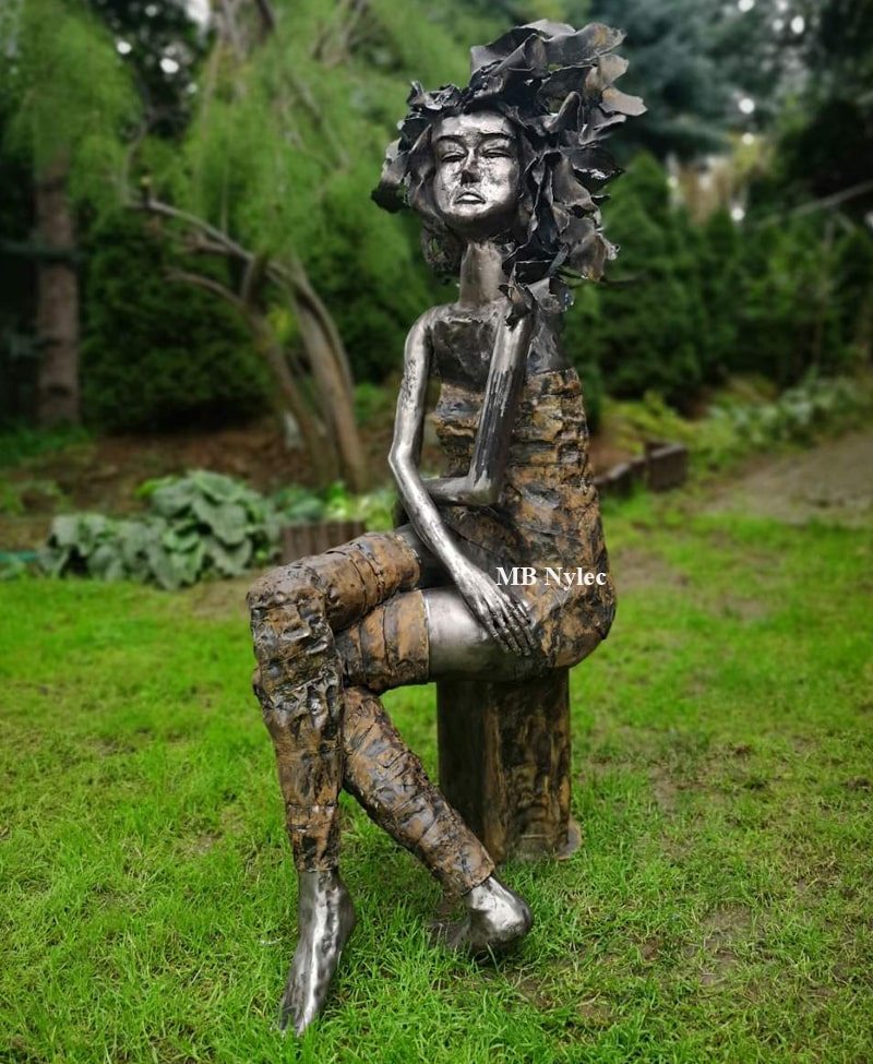 Modern steel sculpture of an elegant seated woman in a garden