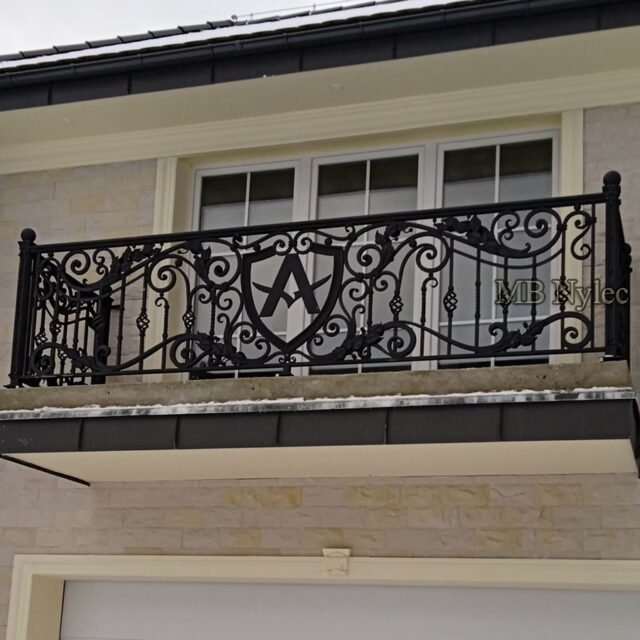 Forged balcony railing with a central monogram shield on a villa