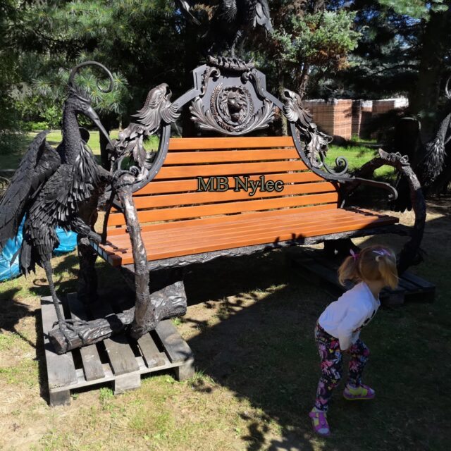 Forged sculpted bench with a child standing beside it for scale