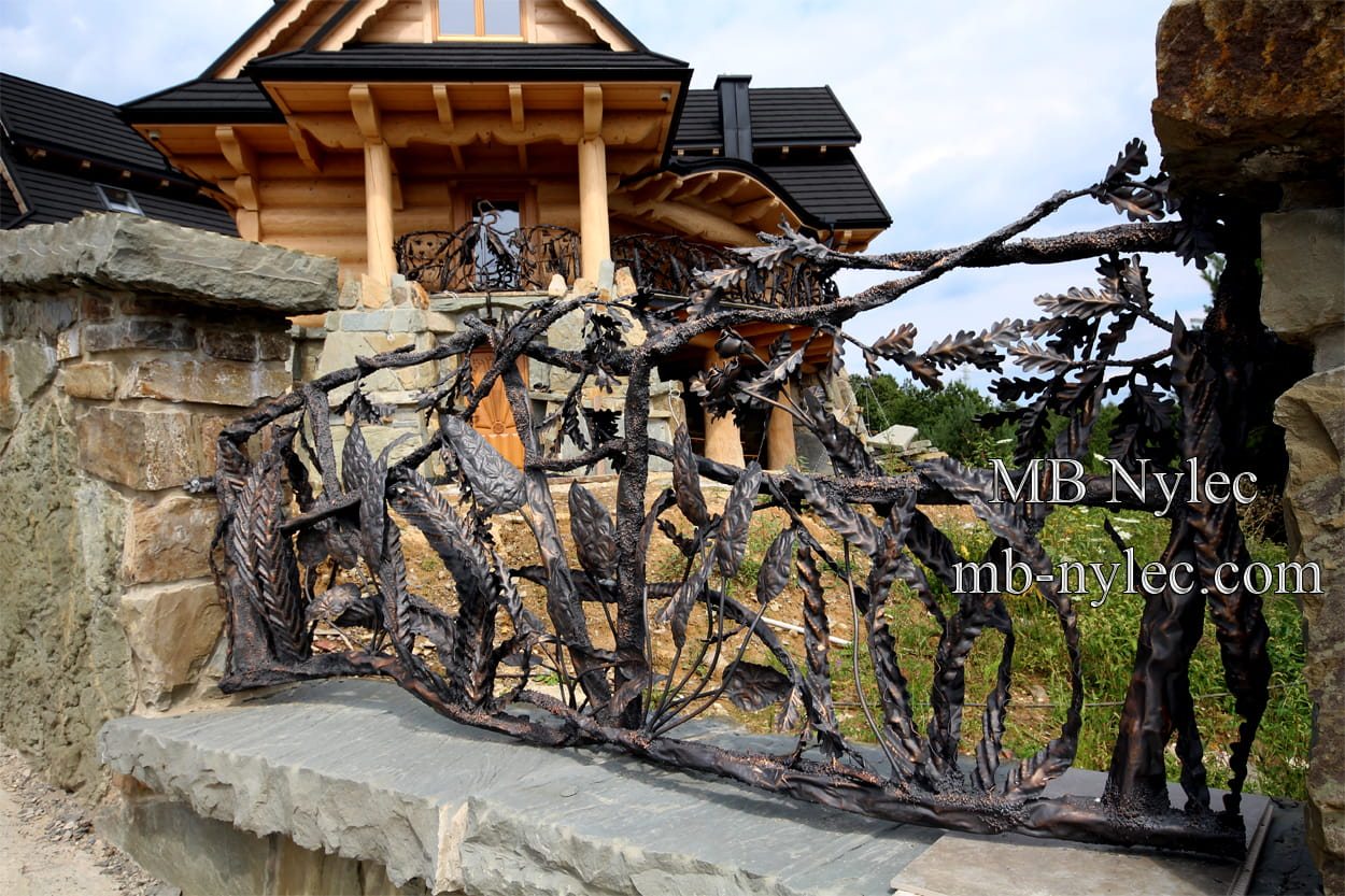 Forged branch fence on a fieldstone wall in front of a log home