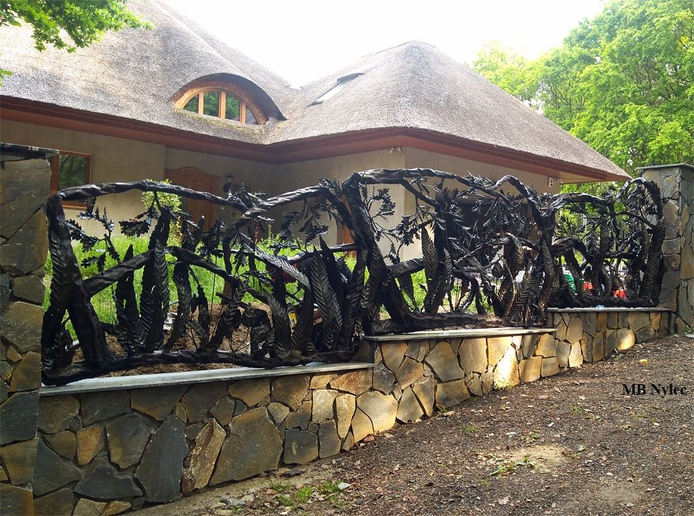 Forged forest fence in highland style in front of a thatched-roof house