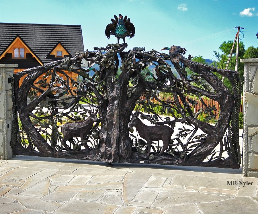 Forged highland driveway gate with a capercaillie on top in front of a log home