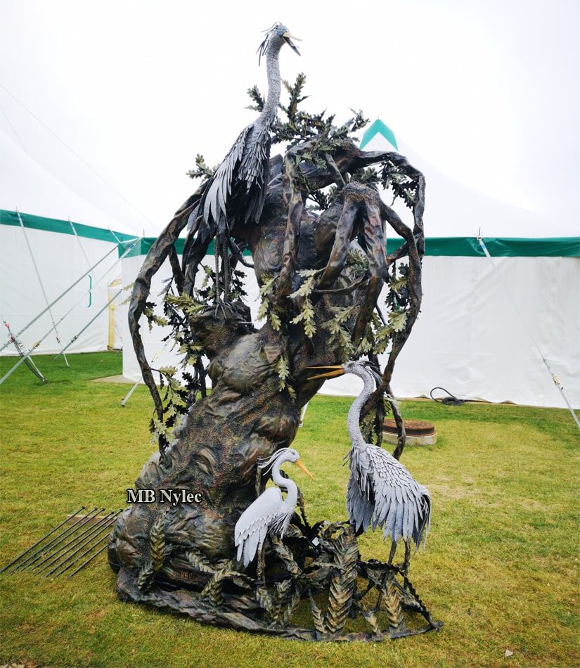 Forged lamp with several steel herons among the roots