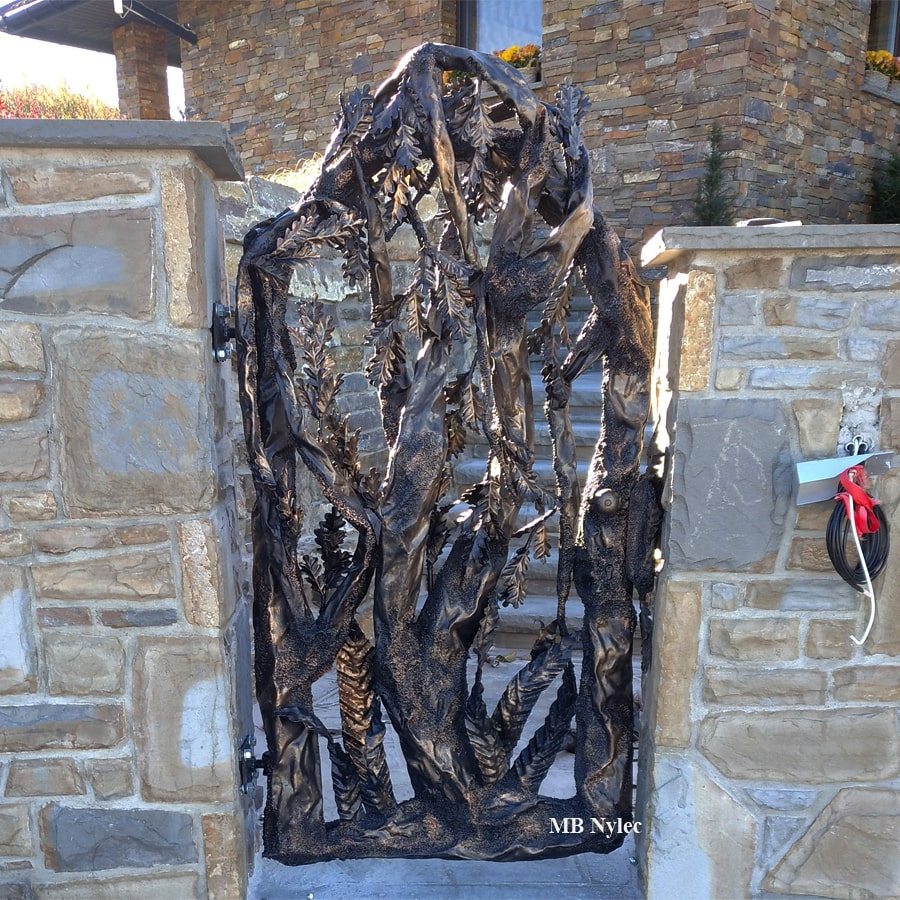 Hand-forged steel wicket gate shaped like a tree set into a stone wall