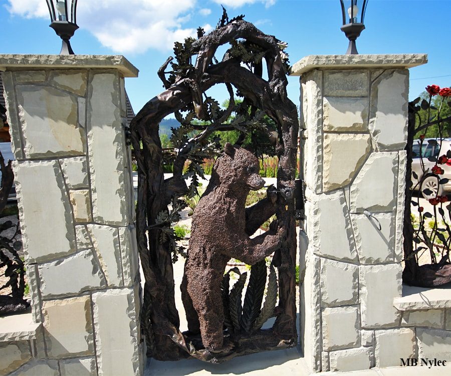 Forged wicket gate with a steel bear between stone pillars with lanterns