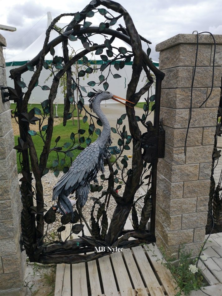 Garden wicket gate with a steel heron among reeds and arching branches