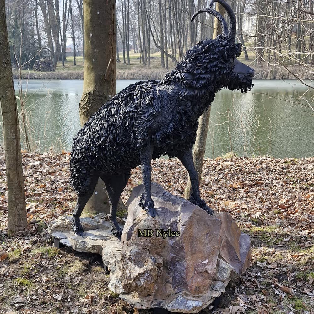 Life-size steel goat sculpture standing on a natural stone by a pond