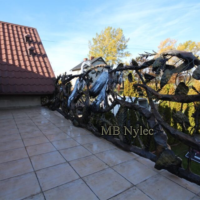 Hand-forged metal railing with herons by a red-roofed house