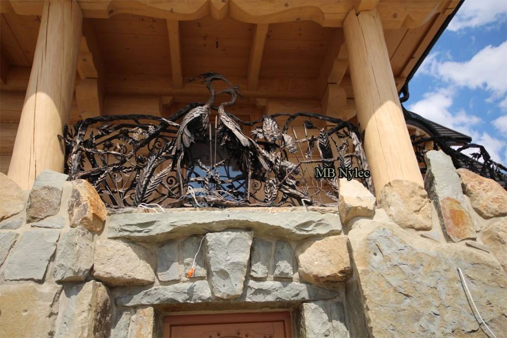 Front view of the forged heron balcony railing BA83 on a stone facade