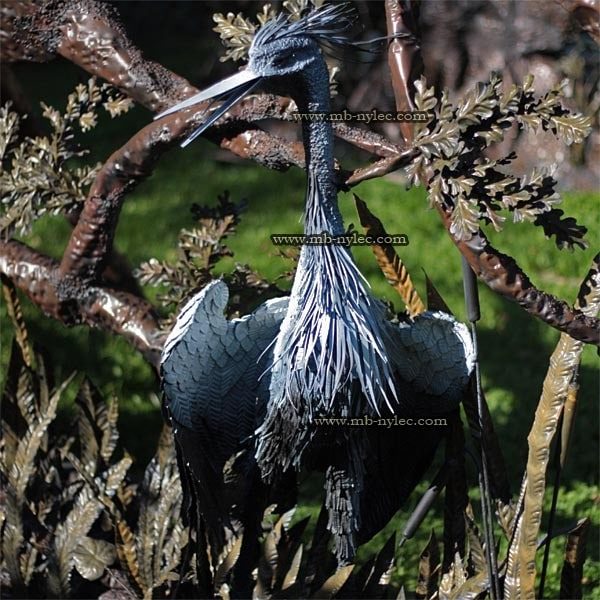 Steel heron Z19 with its beak raised among forged branches