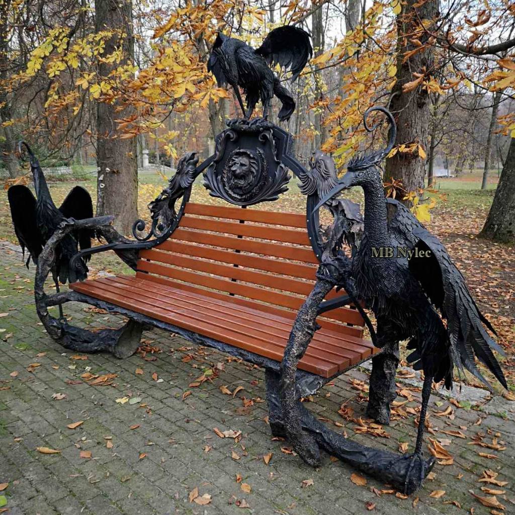 Massive palace forged bench with fairy-tale herons and an oak seat in a park
