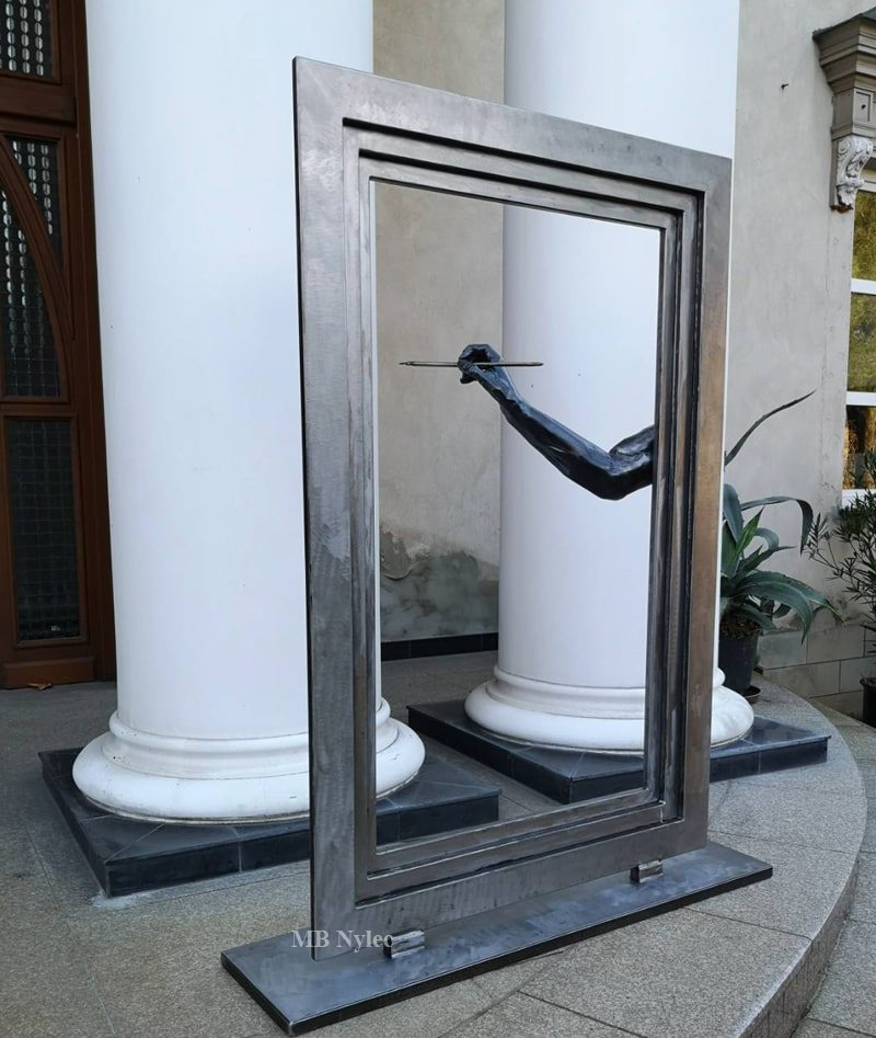 Metal sculpture of a frame and painting hand between white columns