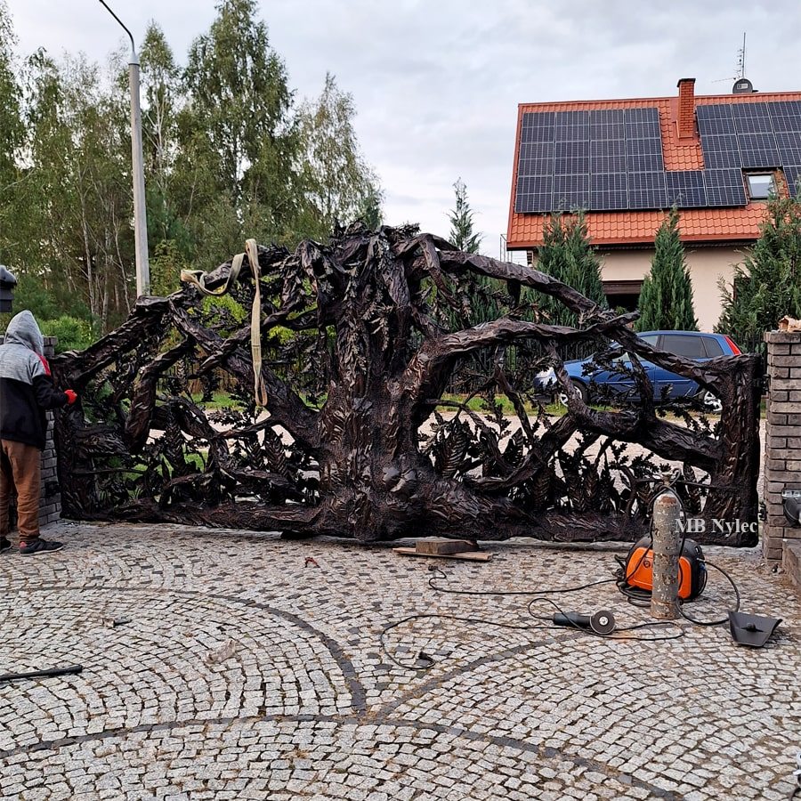 Metal driveway gate forged as a tree in front of a modern house
