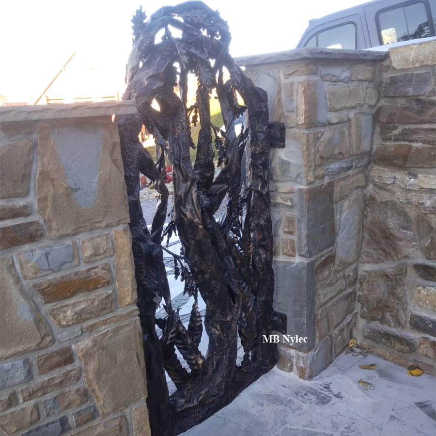 Side view of a metal tree pedestrian gate between stone pillars