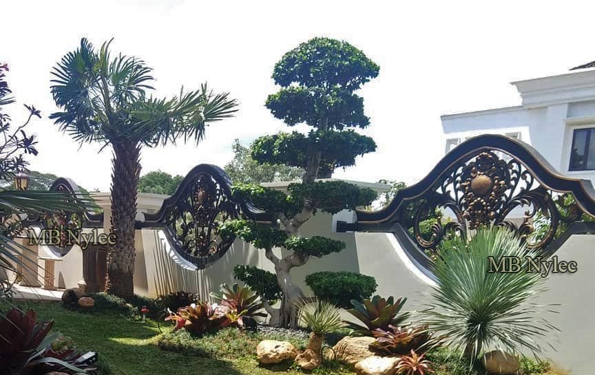 Oriental wrought iron fence BP206 among palms and topiary in a tropical garden