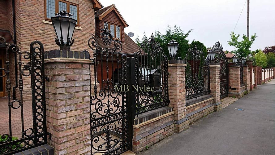 Ornate wrought iron fence BP234 seen along the pavement, with lanterns on brick pillars