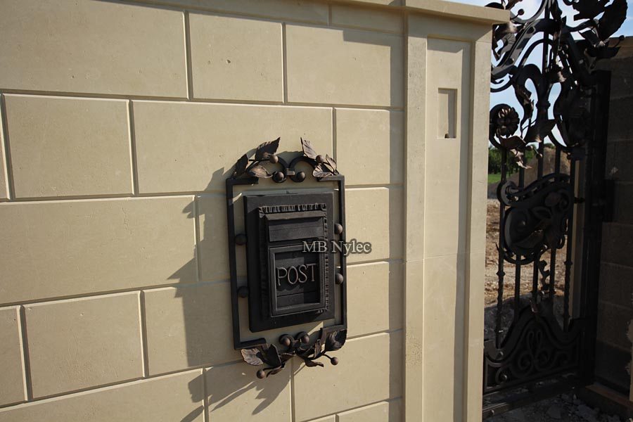 Forged POST letterbox PS1 with leafy branches mounted on a light rendered wall