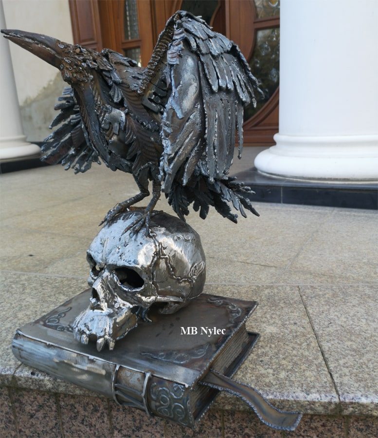 Steel sculpture of a raven with spread wings on a skull and a book