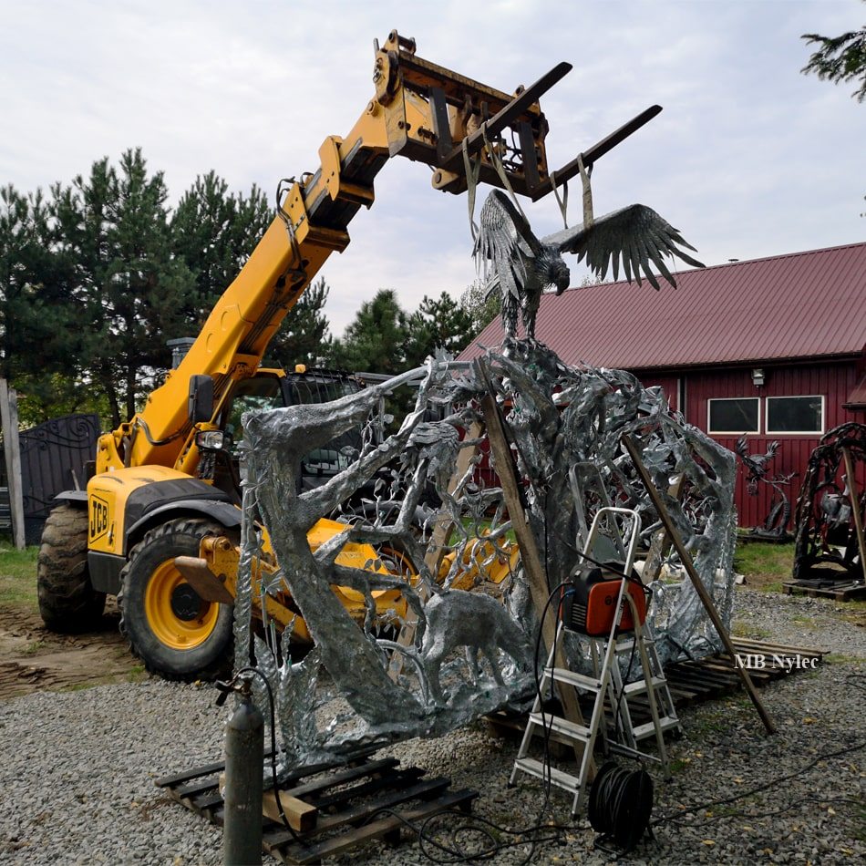 Sculpted steel gate being lifted into place by a telehandler