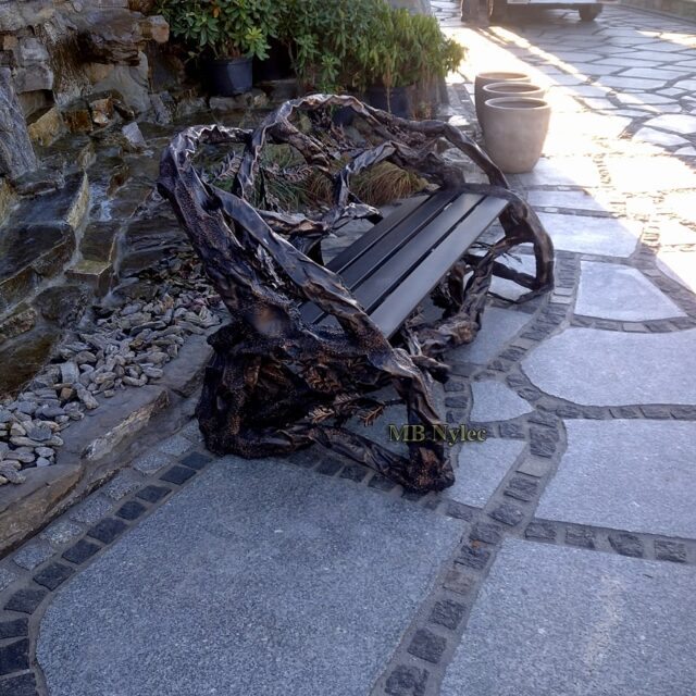Side view of a steel branch bench on stone paving