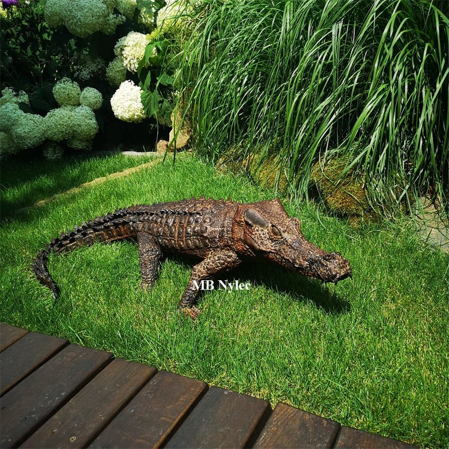 Hand-made steel crocodile Z122 lying on a garden lawn