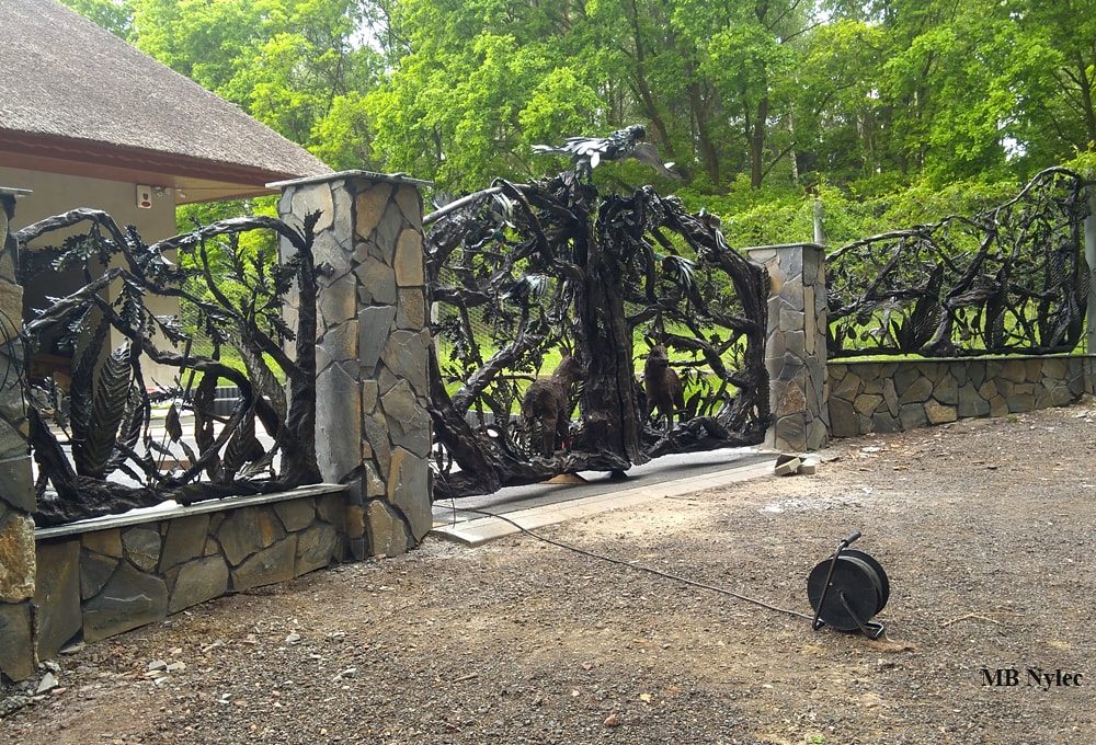 Steel fence with a forged tree between stone pillars