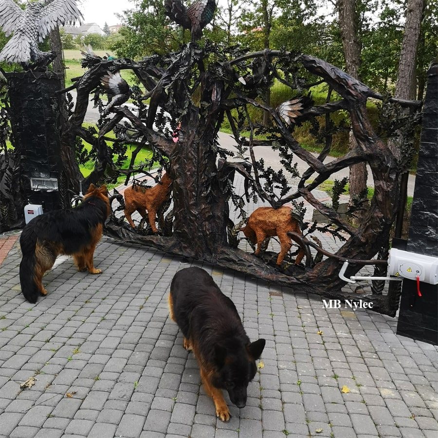 Steel sculpture gate with forest animals and a dog for scale