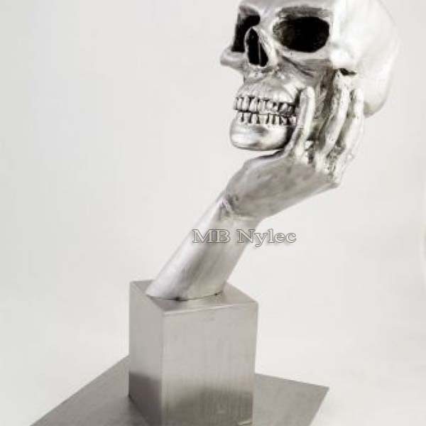 Steel sculpture of a skull resting in a hand rising from a square steel block