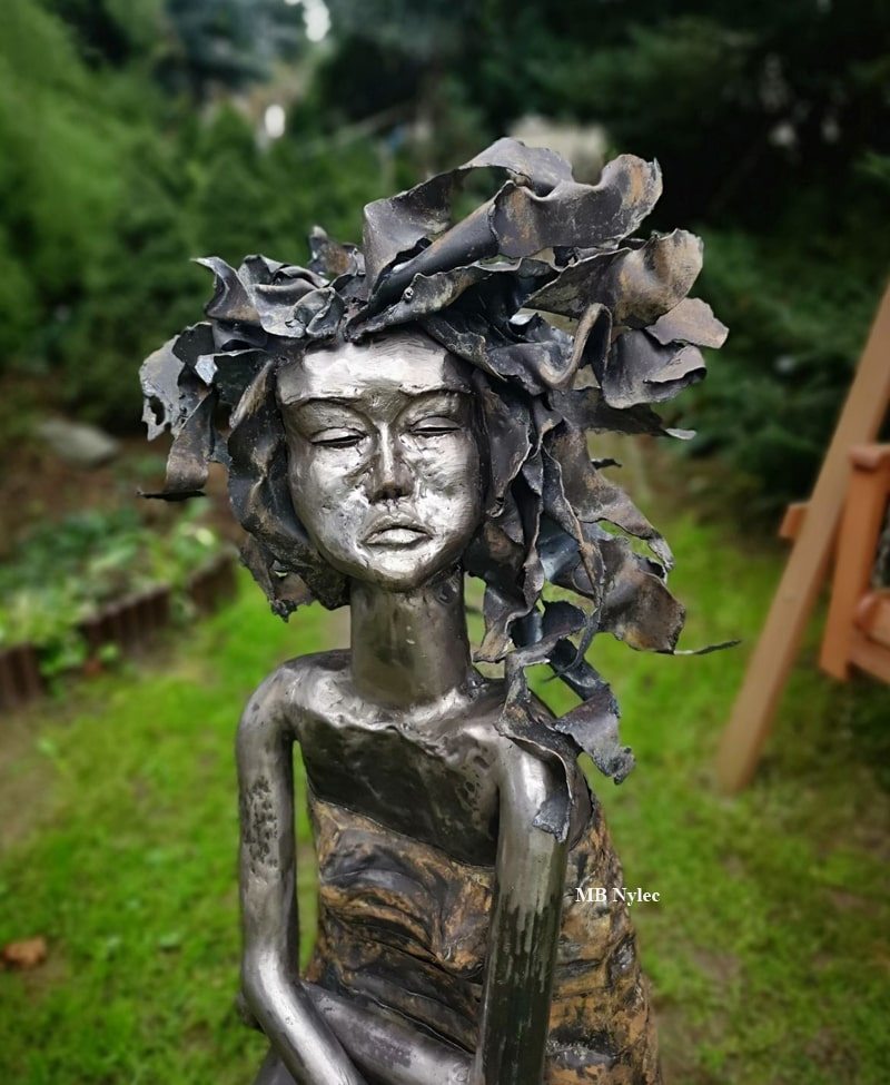 Close-up of a steel woman with hair of curling petals and leaves
