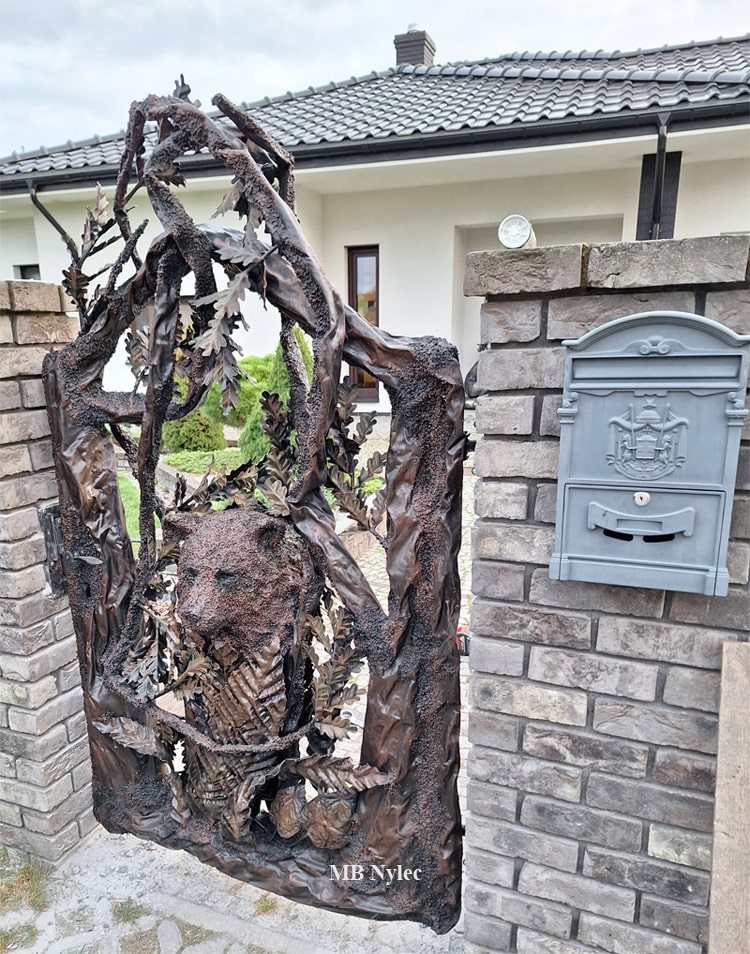 Metal tree wicket gate with a forged bear cub's head between brick pillars